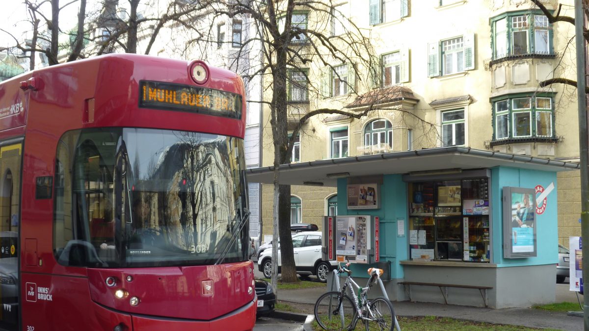 Straße im Innsbrucker Stadtteil Saggen mit Straßenbahn, Fahrrad, den typischen Häusern und einem Kiosk.