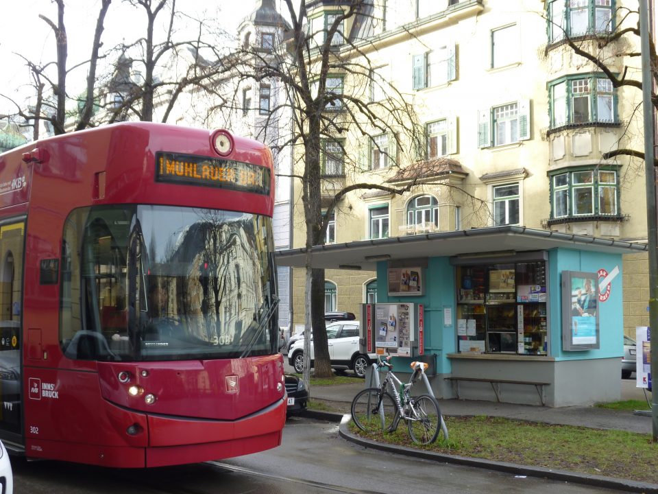 Straße im Innsbrucker Stadtteil Saggen mit Straßenbahn, Fahrrad, den typischen Häusern und einem Kiosk.